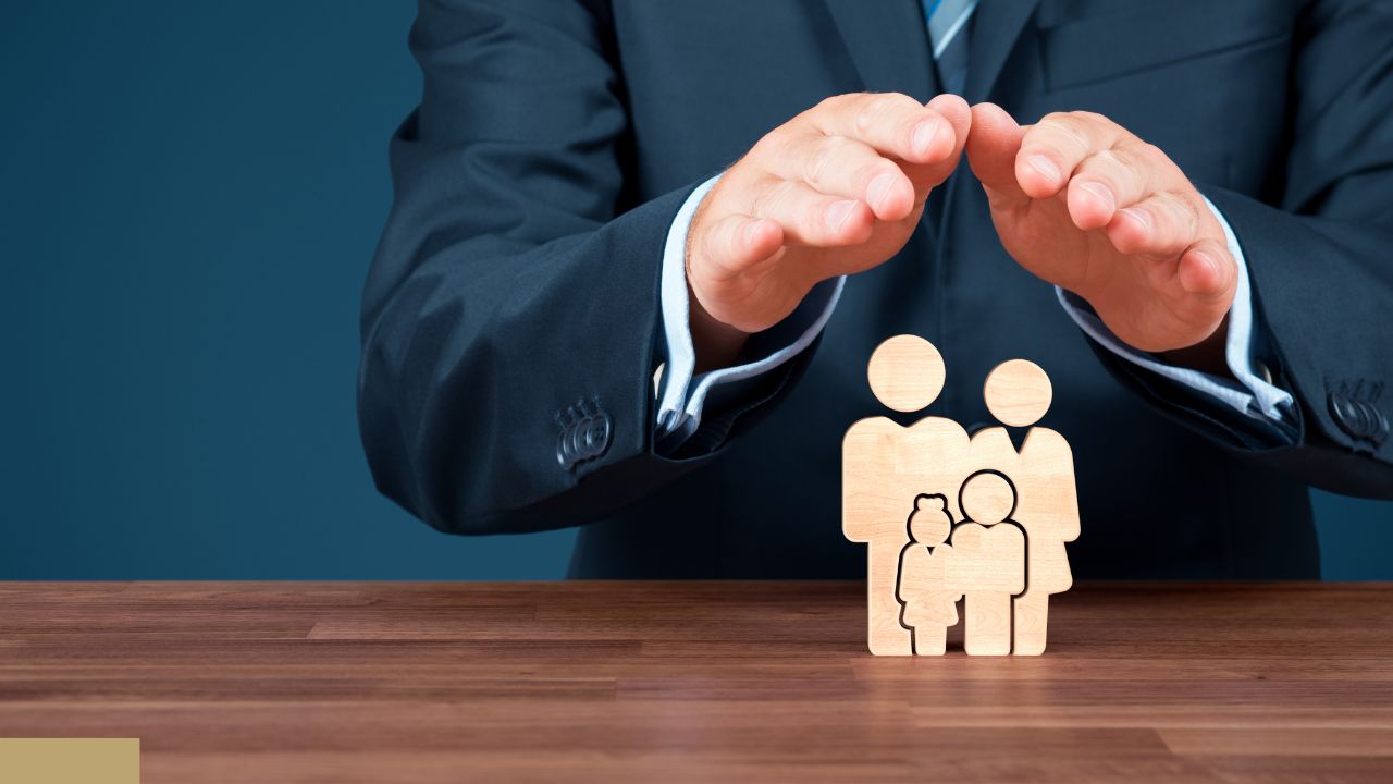 Businessperson in a suit protecting a wooden family icon on a table, symbolizing insurance coverage.