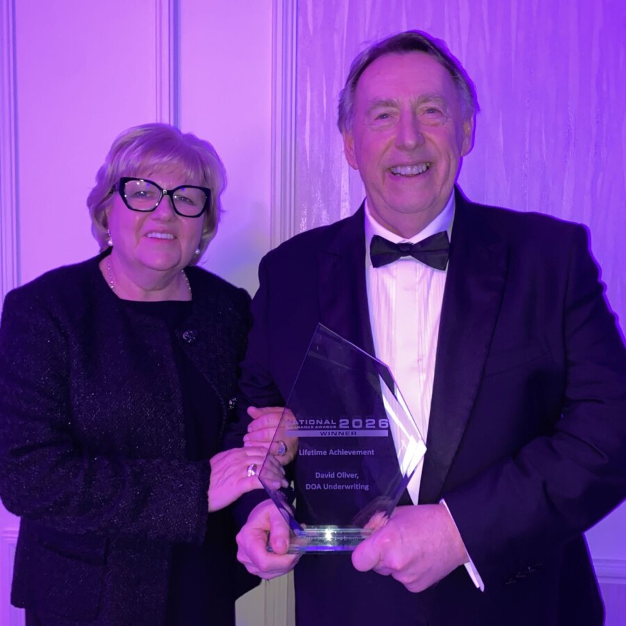 Two people standing together at an awards event holding a glass trophy for a lifetime achievement award.