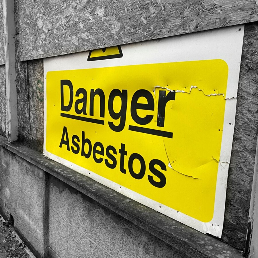 Large yellow “Danger Asbestos” warning sign fixed to a boarded‑up exterior surface, representing hazardous material risks covered by asbestos insurance.