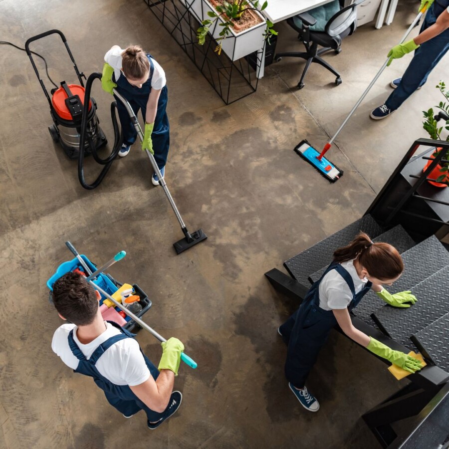 Cleaning team working together to vacuum, mop, and wipe surfaces in a commercial workspace, representing group personal accident insurance.