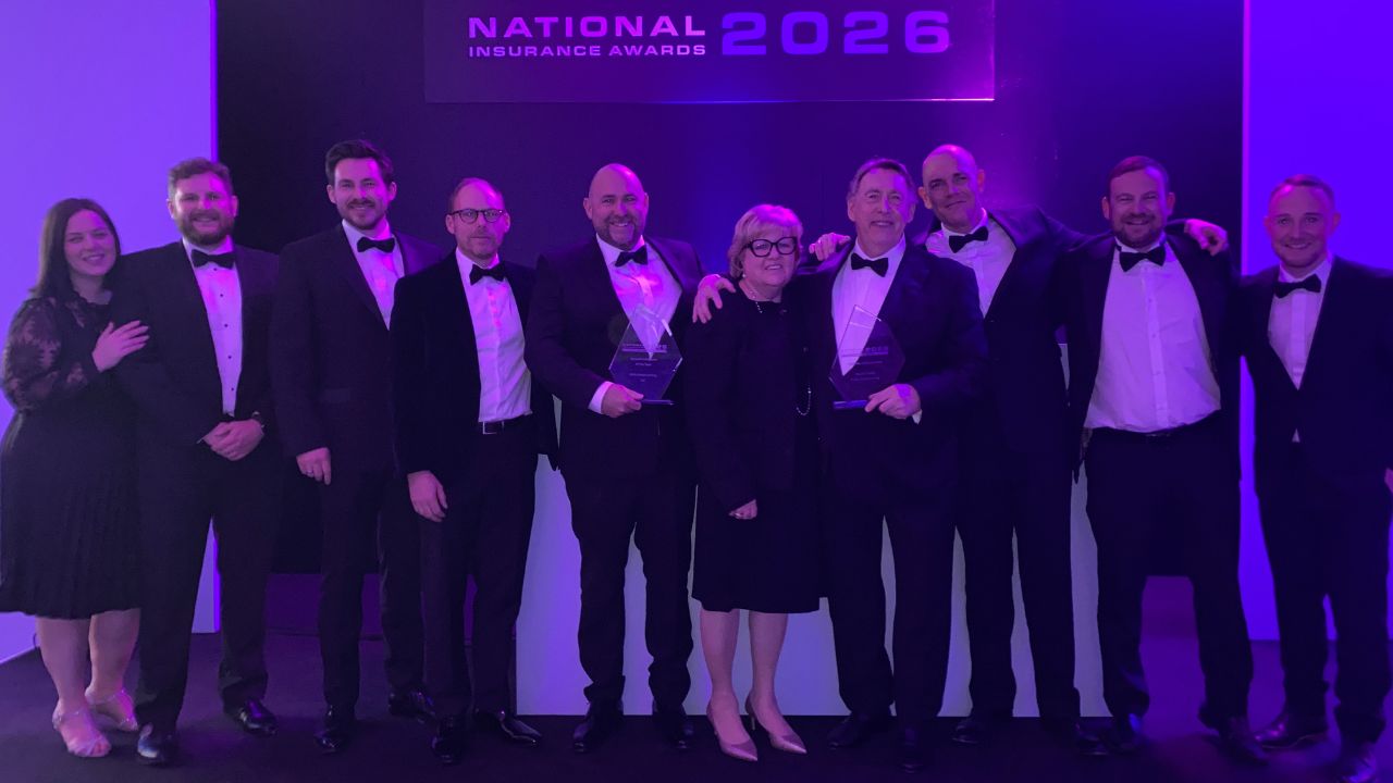 A group of people dressed in formal evening wear standing together on stage at the National Insurance Awards 2026, holding two glass trophies for the lifetime achievement award and growth company of the year.