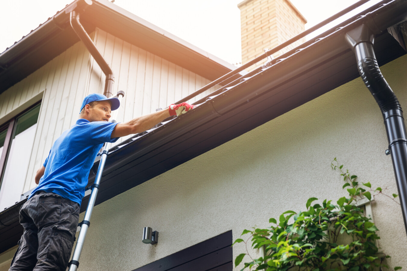 Person standing on a ladder and cleaning house guttering on an exterior wall, representing the risks covered by personal accident and sickness insurance.